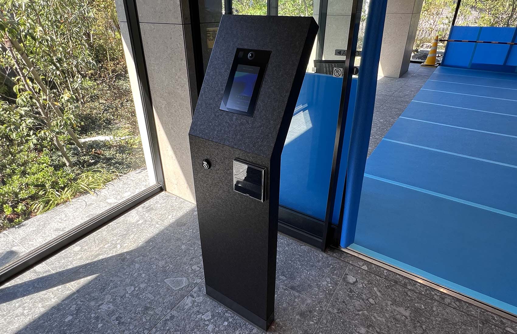 マンション入口のオートロック操作板。 黒い大理石調の自立型のパネルで、操作パネル面が少し斜めに傾いている。