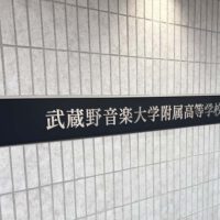 壁面についている、L字型プレート型館銘板。曲げは左側。一面黒いプレートの中央に、ステンレスの切文字の物件名がある。