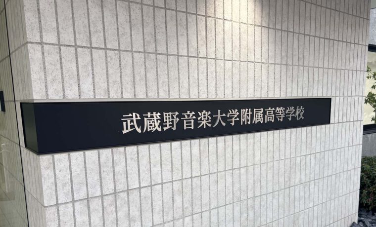 壁面についている、L字型プレート型館銘板。曲げは左側。一面黒いプレートの中央に、ステンレスの切文字の物件名がある。