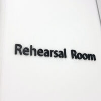 白い壁についている、黒のアクリル切文字室名表示。「Rehearsal Room」と書かれている。