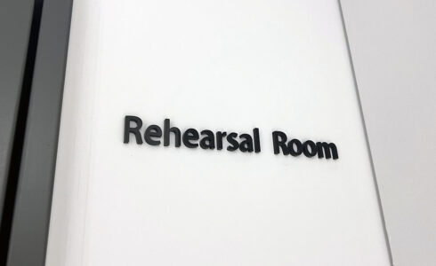 白い壁についている、黒のアクリル切文字室名表示。「Rehearsal Room」と書かれている。